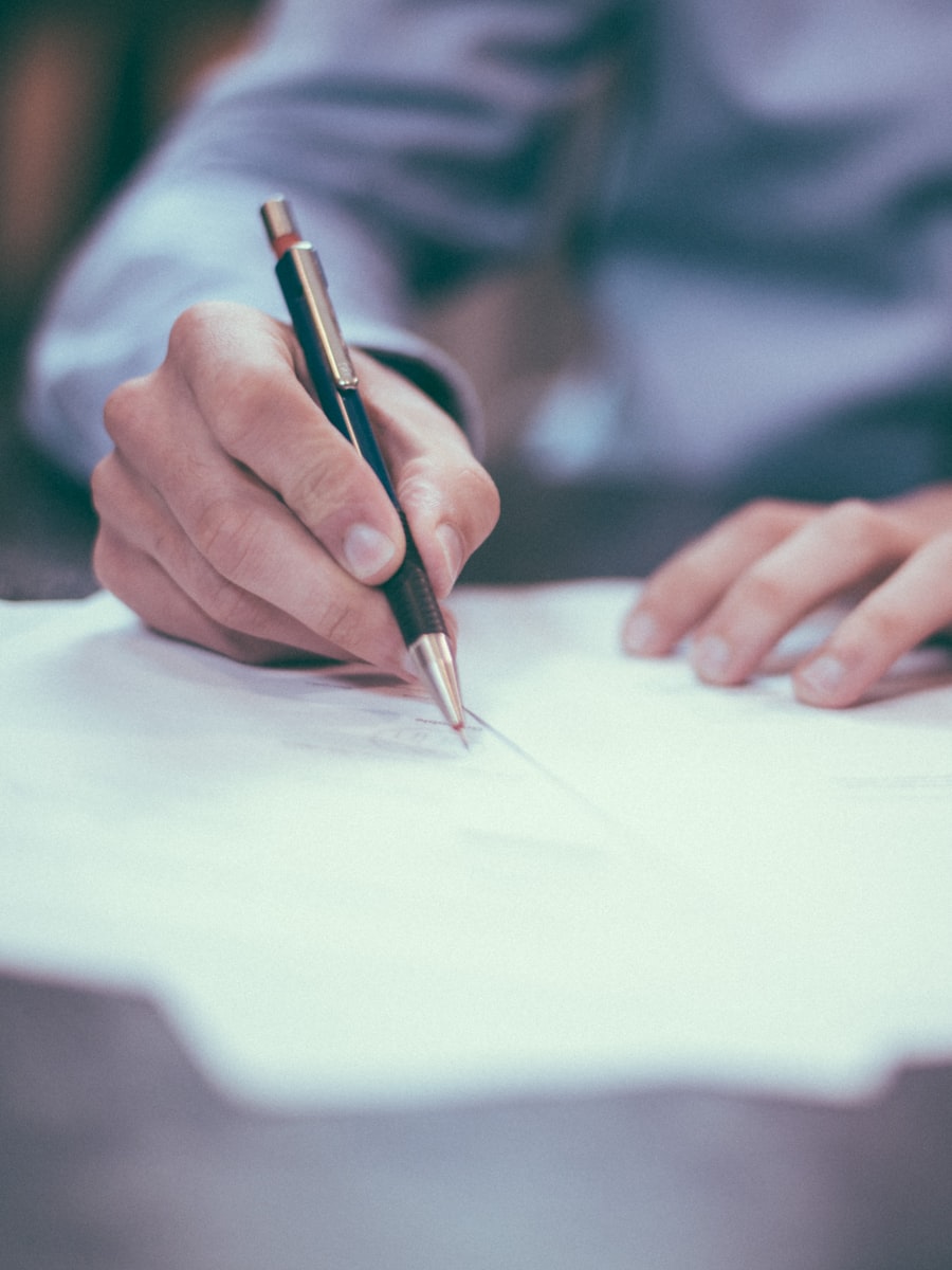 A hand signing a document with a pen at a desk in soft daylight