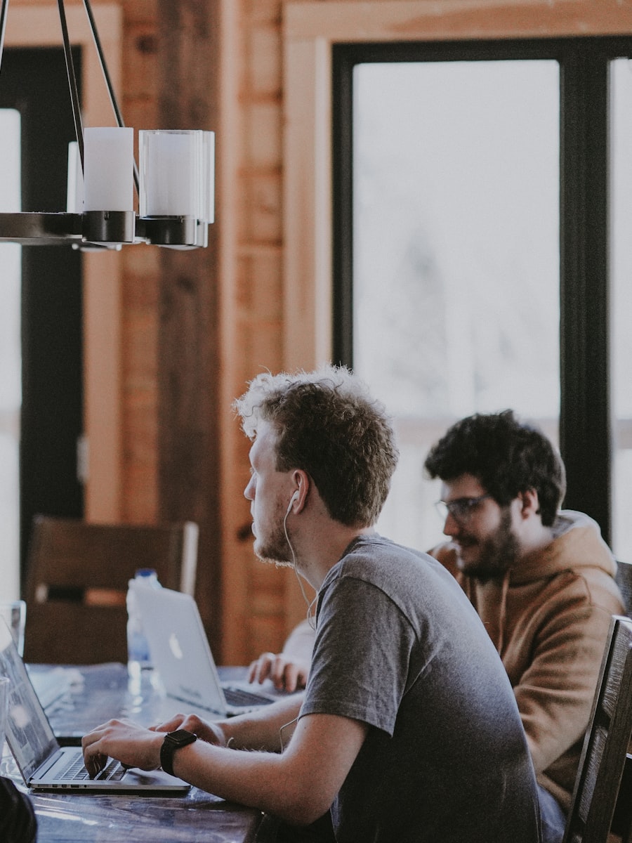 Two colleagues working on laptops at a wooden table in warm light
