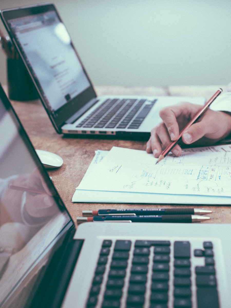 A hand sketching a plan on paper beside a laptop